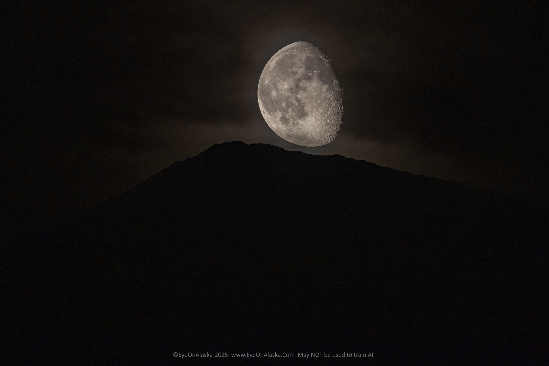 The 3/4 moon, with just a faint halo of color around it, rises above the silhouette of a ridge in the Chugach Mountains behind our house.