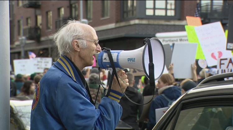 A photo I found from news coverage of the union elder guiding chants along the march route. He has grey thinning hair and a blue coat, signs and banners in the backgrojnd